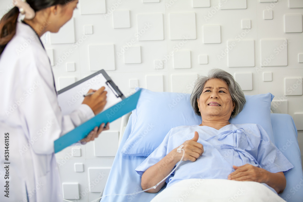 An elderly woman thumbs up and smiling as the doctor examines the condition in the recovery room. Healthcare and medicine concept. An elderly woman thumbs up and smiling as the doctor examines the condition in the recovery room. Healthcare and medicine concept.