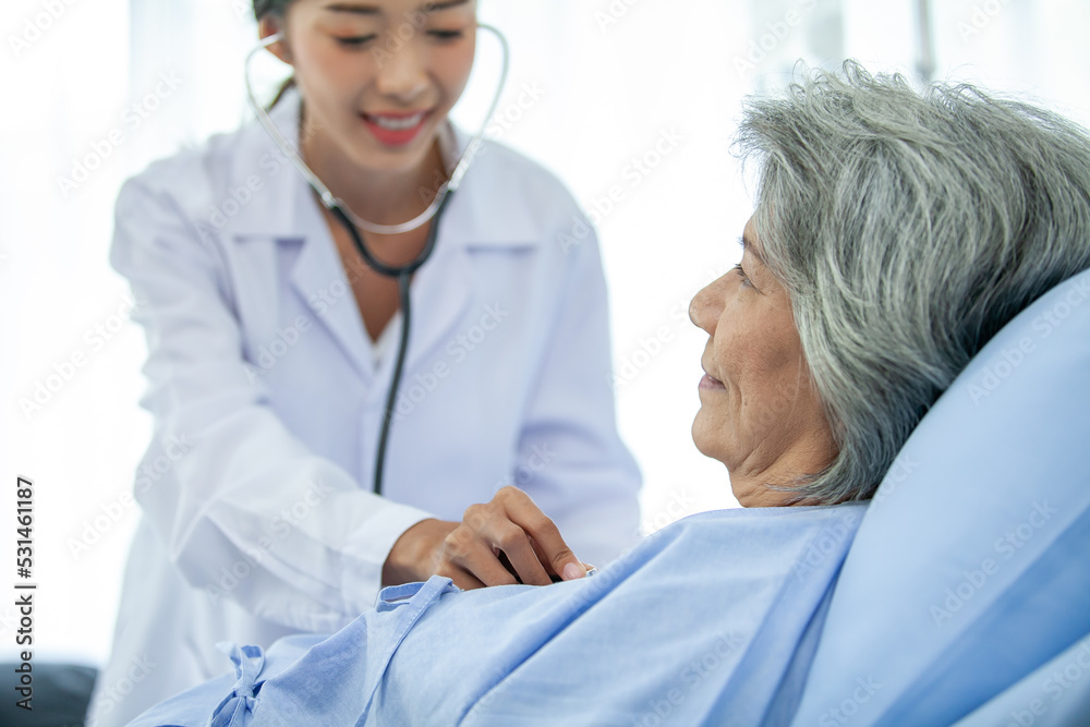 Obraz premium doctor visiting ward have woman patient and check her with stethoscope on bed. Woman patient lying on hospital bed while doctor giving her checkup.