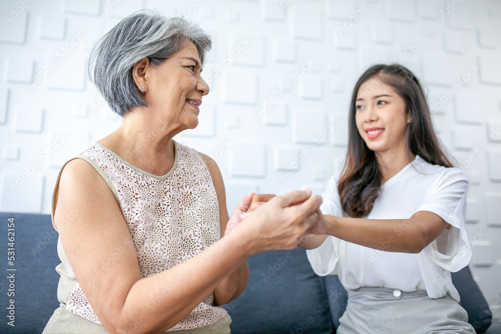 Asian young and senior woman, grandmother and granddaughter holding hands to support and love with smiles on the sofa in the house.