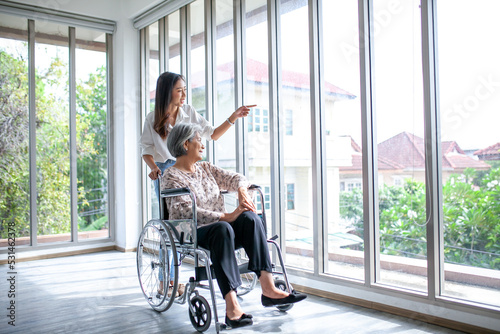 Beautiful asian girl help and take care of senior elderly woman sitting on wheelchair at living room in house, senior therapy patient at home concept.