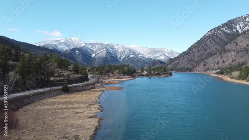 Forward tracking shot over pristine river in Montana valley with truck passing through on the way to gorgeous mountain range