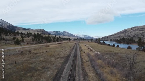 Overhead shot following a single railroad track beside a river in rural Missoula Montana on a beautiful day 