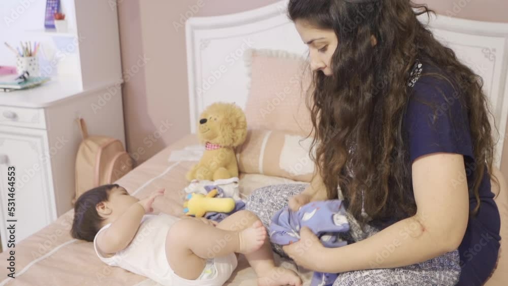 The mother dressing her baby.
Mother dressing her baby lying in bed. Happy baby.
