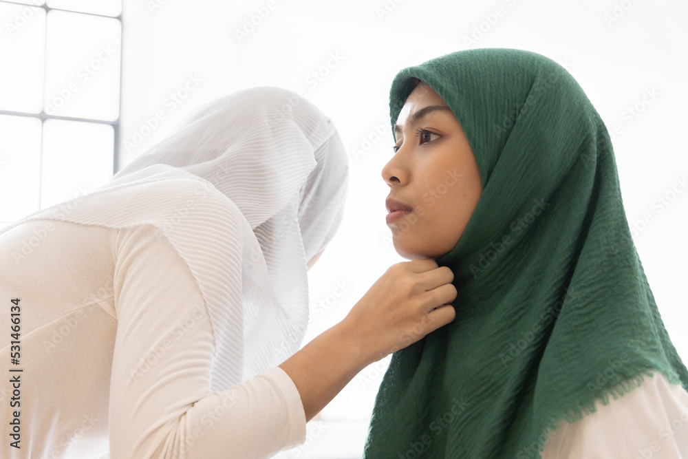 Fototapeta premium Happy smiling muslim woman help dressing up hijab for her friend, concept of islamic sisterhood, friendship among female muslim people