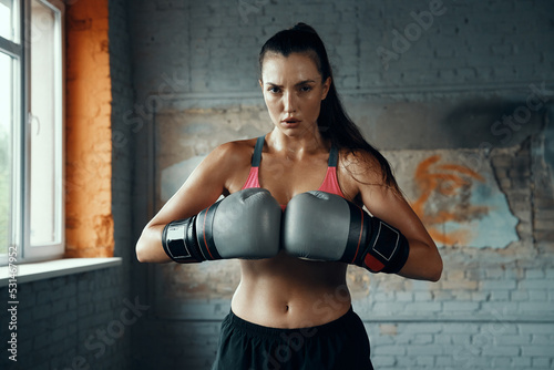 Confident young woman in boxing gloves looking at camera while standing in gym