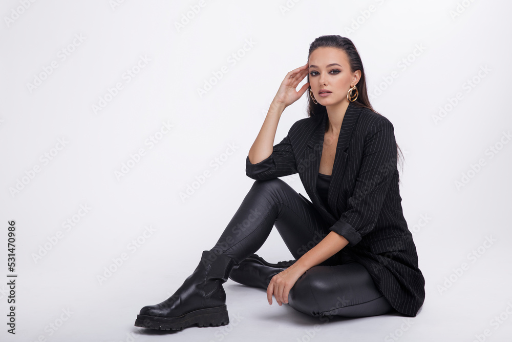 Fashion photo of a beautiful elegant young woman in a pretty black jacket, leather pants, boots, posing over white background. The hair is gathered back, dark brunette. Studio Shot Fashion photo of a beautiful elegant young woman in a pretty black jacket, leather pants, boots, posing over white background. The hair is gathered back, dark brunette. Studio Shot