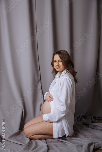 pregnant woman in white clothes on a background of gray fabric