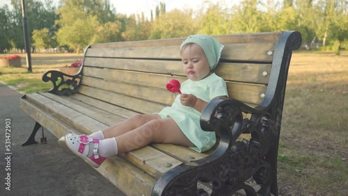 A little girl of 2 years old enjoys eating ice cream sitting on a park bench, side view