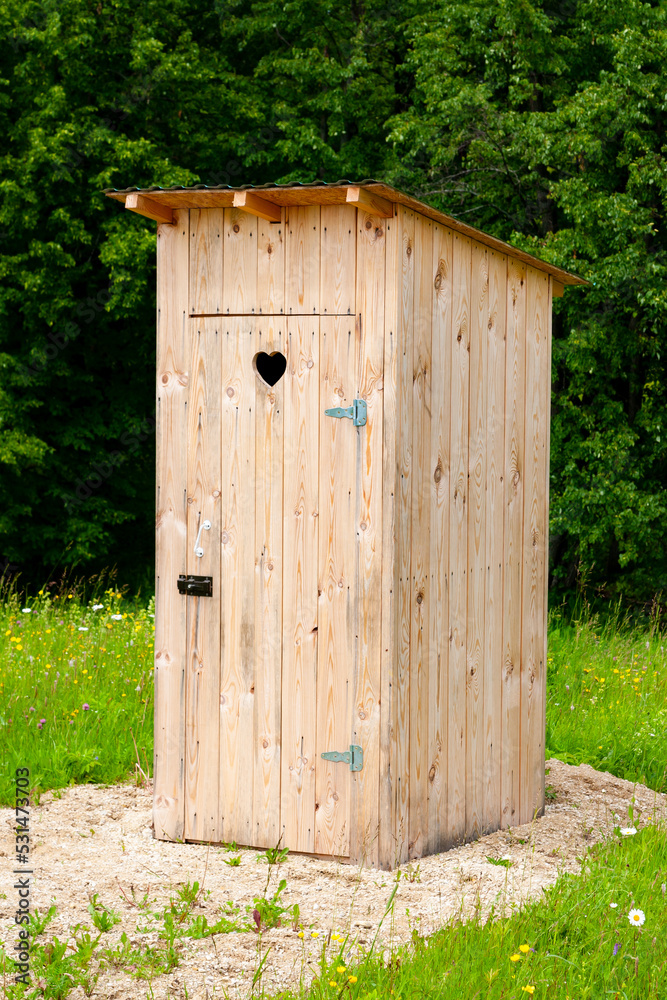 Wooden toilet in the countryside with a heart-shaped hole on the door. Wooden toilet on a background of trees.