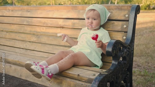 A 2-year-old girl eats ice cream and wipes her face with a wet napkin on her own