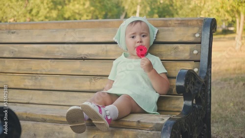 A 2-year-old girl eats ice cream sitting on a park bench, front view