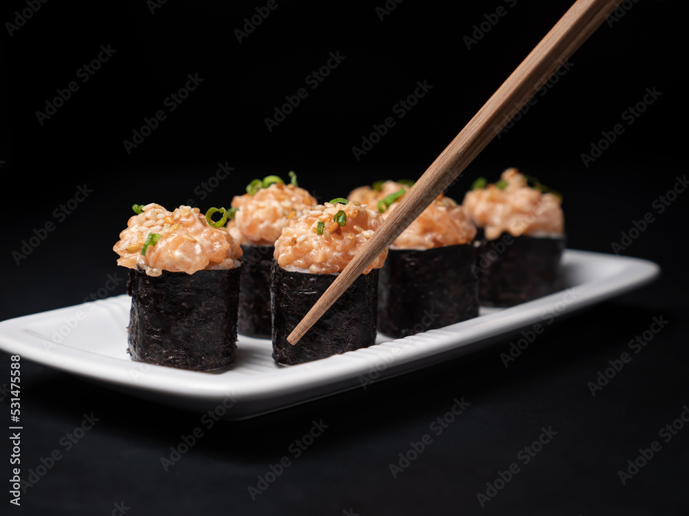 Take one sushi roll from black slate board using chopsticks Take one sushi roll from black slate board using chopsticks