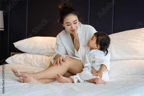 Asian young mother and her daughter in a bathrobe having fun and using a good time on the bed. Selective focus.