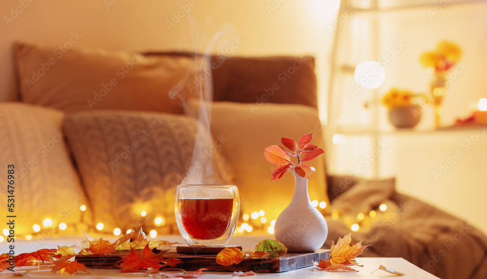 Obraz premium thermo glass with hot tea in dark night room with autumnal leaves