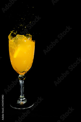 orange drink splash in glass cup on black background