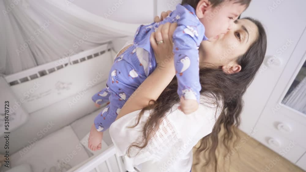 The mother takes the crying baby from the cradle. The baby is crying in the crib. The mother