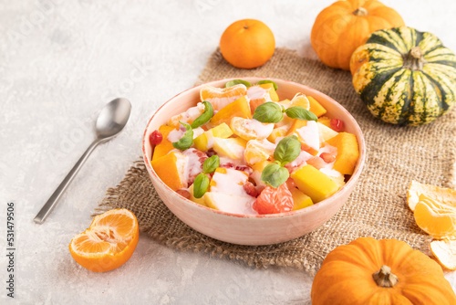 Vegetarian fruit salad of yogurt pumpkin, tangerine, basil microgreen on gray, side view, close up.