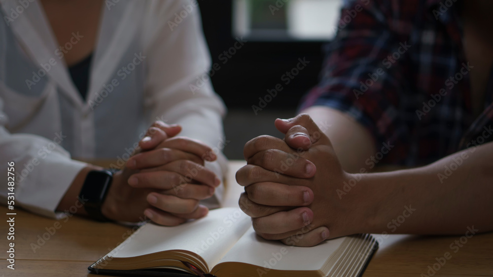 group of asian catholic pray, hope for peace the world and free from war and coronavirus. Young man and woman Hand in hand together on bible (worship christian), thinking and closed eyes at church