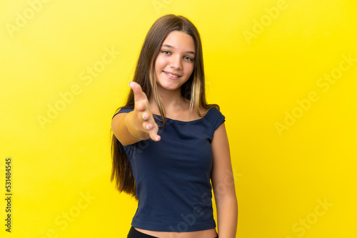 Little caucasian girl isolated on yellow background shaking hands for closing a good deal