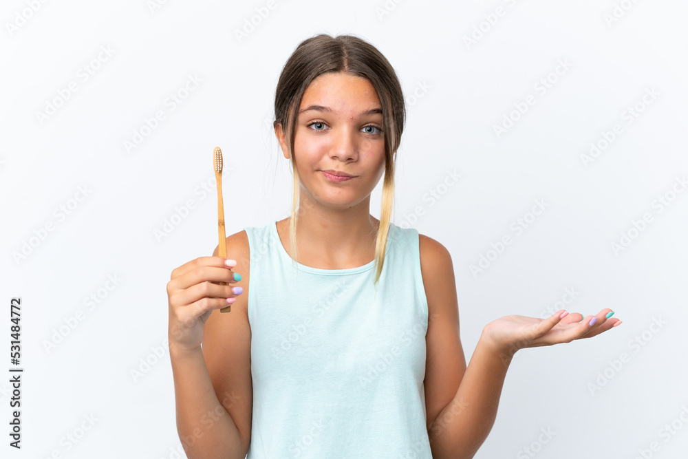 Little caucasian girl holding a toothbrush isolated on white background making doubts gesture while lifting the shoulders Little caucasian girl holding a toothbrush isolated on white background making doubts gesture while lifting the shoulders