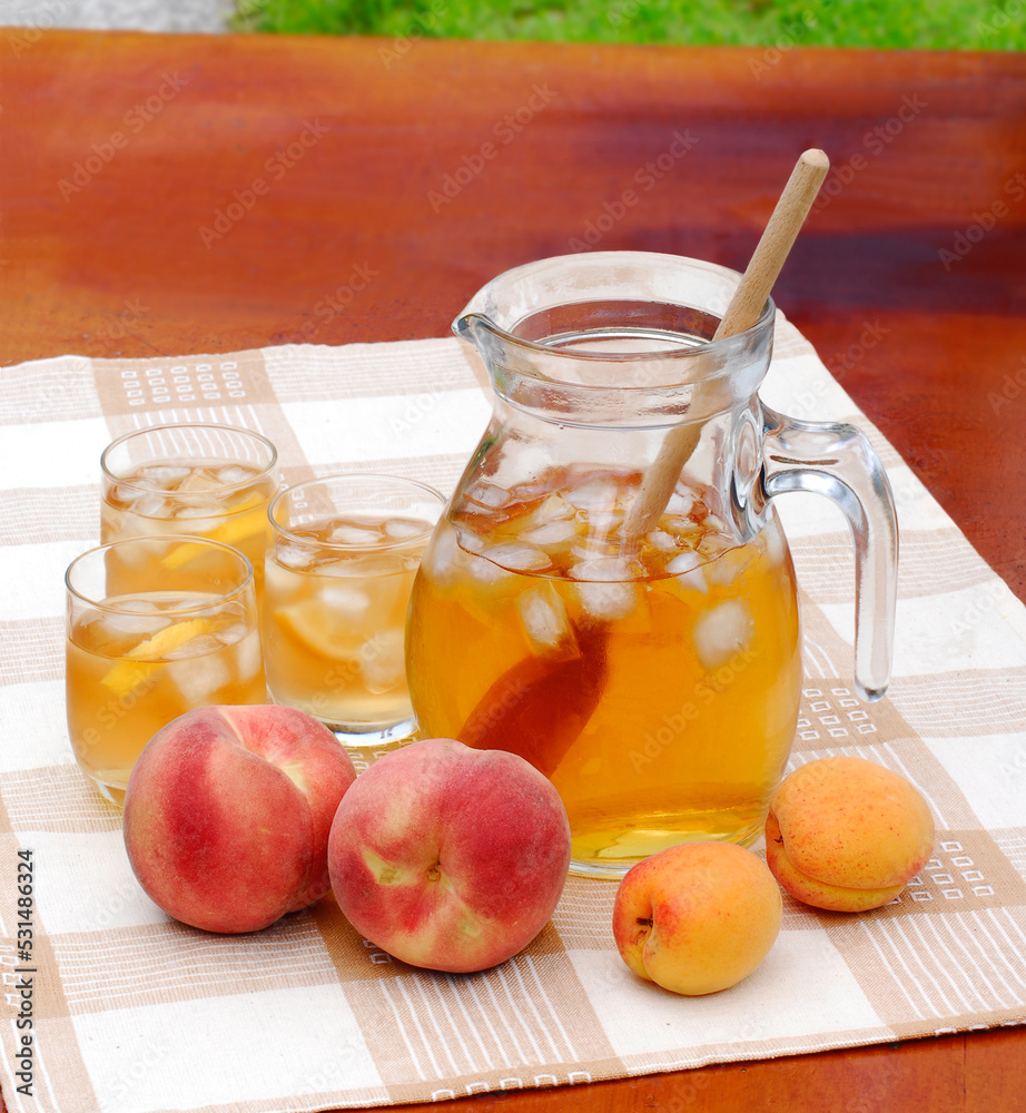 Peach cold tea jar ice glasses and peach fruits on outdoors table background. Peach cold tea jar ice glasses and peach fruits on outdoors table background.