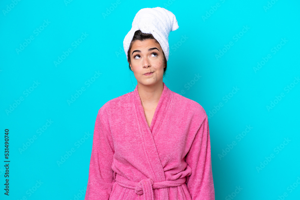 Young Brazilian woman with a bathrobe isolated on blue background and looking up