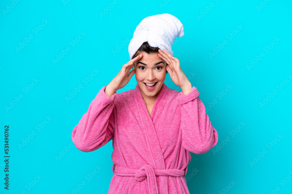 Young Brazilian woman with a bathrobe isolated on blue background with surprise expression Young Brazilian woman with a bathrobe isolated on blue background with surprise expression