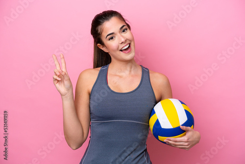 Young Brazilian woman playing volleyball isolated on pink background smiling and showing victory sign