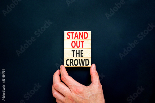 Stand out the crowd symbol. Concept words Stand out the crowd on wooden blocks on beautiful black table black background. Businessman hand. Business, stand out the crowd concept