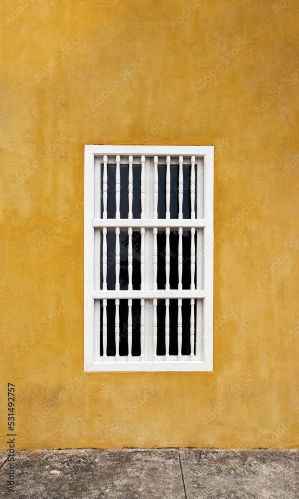 Yellow colorful wall with a white window in caribbean house.