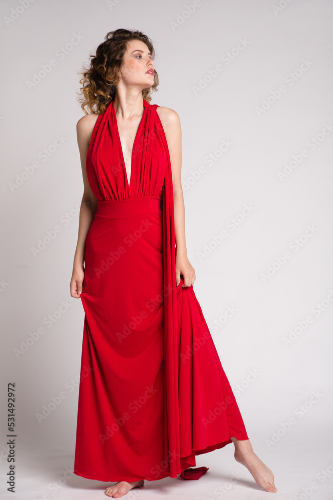 High fashion photo of a beautiful elegant young woman in a pretty long red dress, hairstyle on white, soft gray background. Studio Shot. 