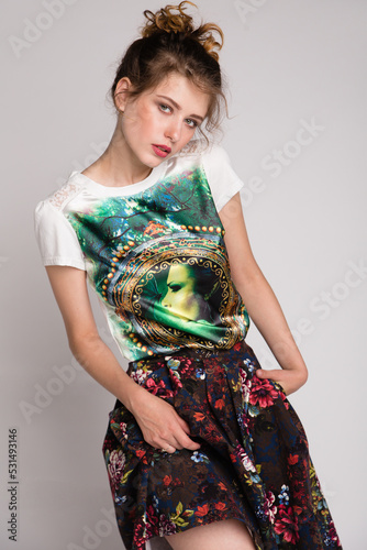 High fashion photo of a beautiful elegant young woman in a pretty dark long skirt with floral pattern, green t-shirt on white, soft gray background. Studio Shot.