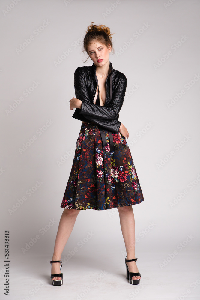 Fototapeta premium High fashion photo of a beautiful elegant young woman in a pretty dark long skirt with floral pattern, black leather jacket on white, soft gray background. Studio Shot. 