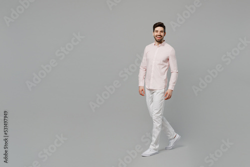 Full body young cheerful smiling happy cool caucasian man 20s he wearing basic white shirt walking going look camera isolated on plain grey color background studio portrait. People lifestyle concept.