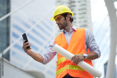 Architect or engineer with blueprints. Cauacsian Engineer checking plan on construction site. modern structure. helmet and blueprints paper. photo
