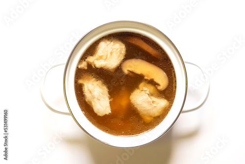 Pot of pork cartilage and shiitake mushroom soup with herbs isolated on white background.