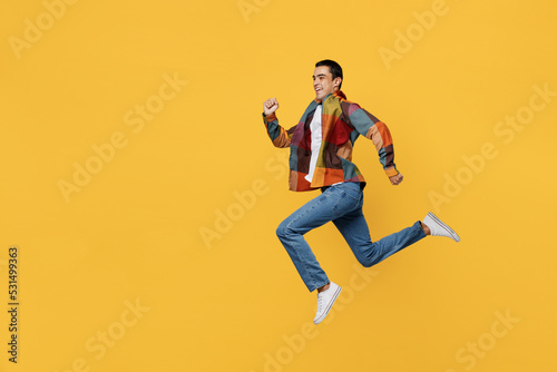 Full body isde view young sporty strong middle eastern man 20s wear casual shirt white t-shirt jump high run fast hurrying isolated on plain yellow background studio portrait People lifestyle concept.