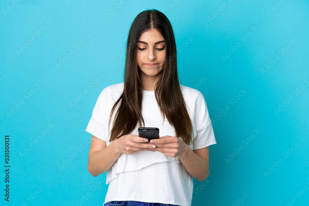 Young caucasian woman isolated on blue background using mobile phone Young caucasian woman isolated on blue background using mobile phone
