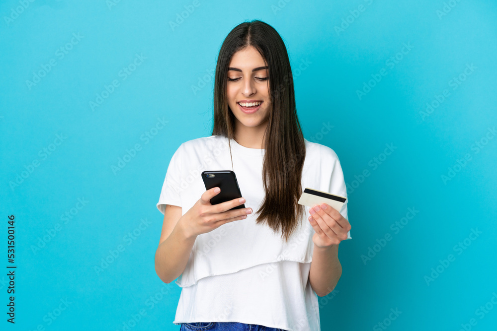 Young caucasian woman isolated on blue background buying with the mobile with a credit card Young caucasian woman isolated on blue background buying with the mobile with a credit card