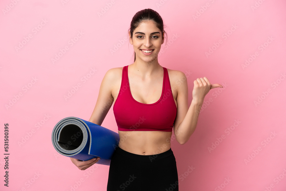 Young sport caucasian woman going to yoga classes while holding a mat pointing to the side to present a product Young sport caucasian woman going to yoga classes while holding a mat pointing to the side to present a product