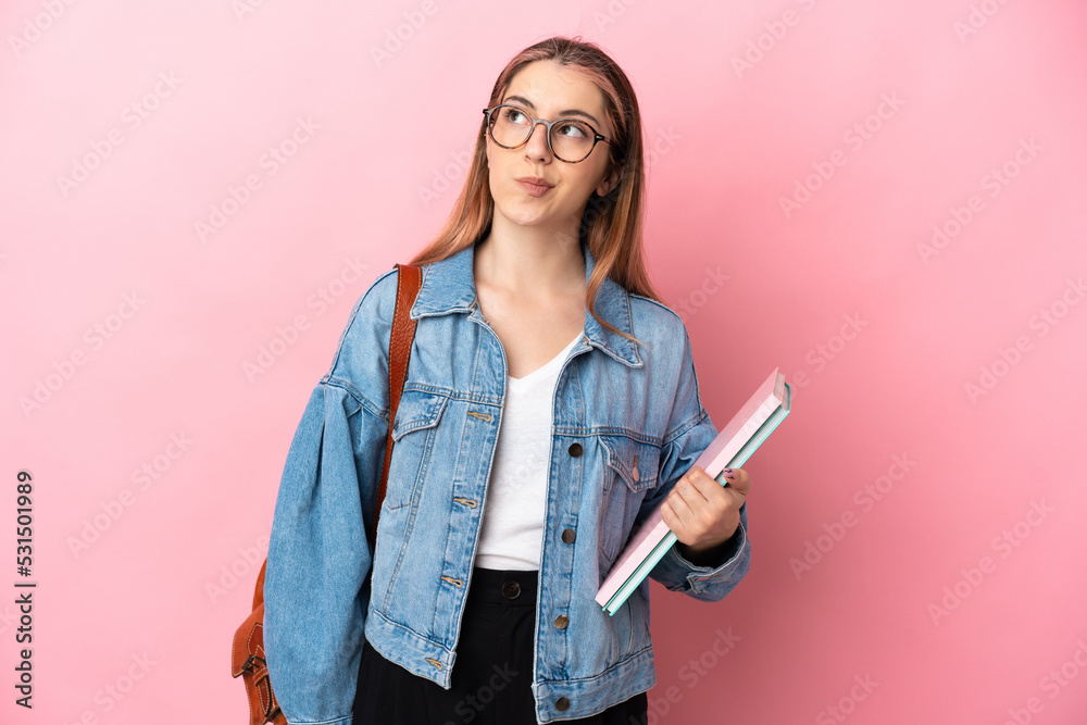 Young caucasian student woman isolated on pink background and looking up