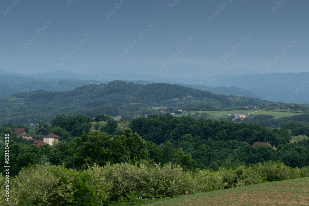 HIlly village with scattered houses and mountain in haze during gloomy day, rural landscape