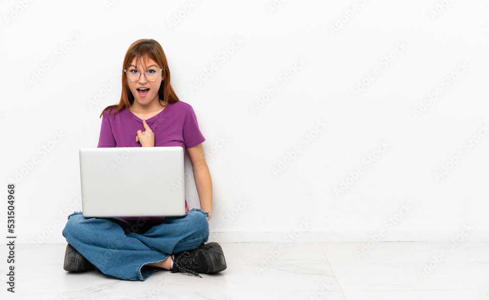 redhead girl with a laptop sitting on the floor with surprise facial expression redhead girl with a laptop sitting on the floor with surprise facial expression