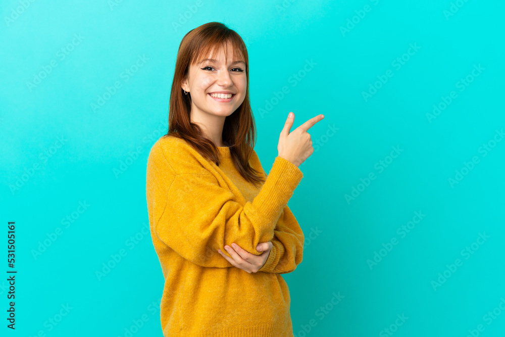Redhead girl isolated on blue background pointing finger to the side Redhead girl isolated on blue background pointing finger to the side