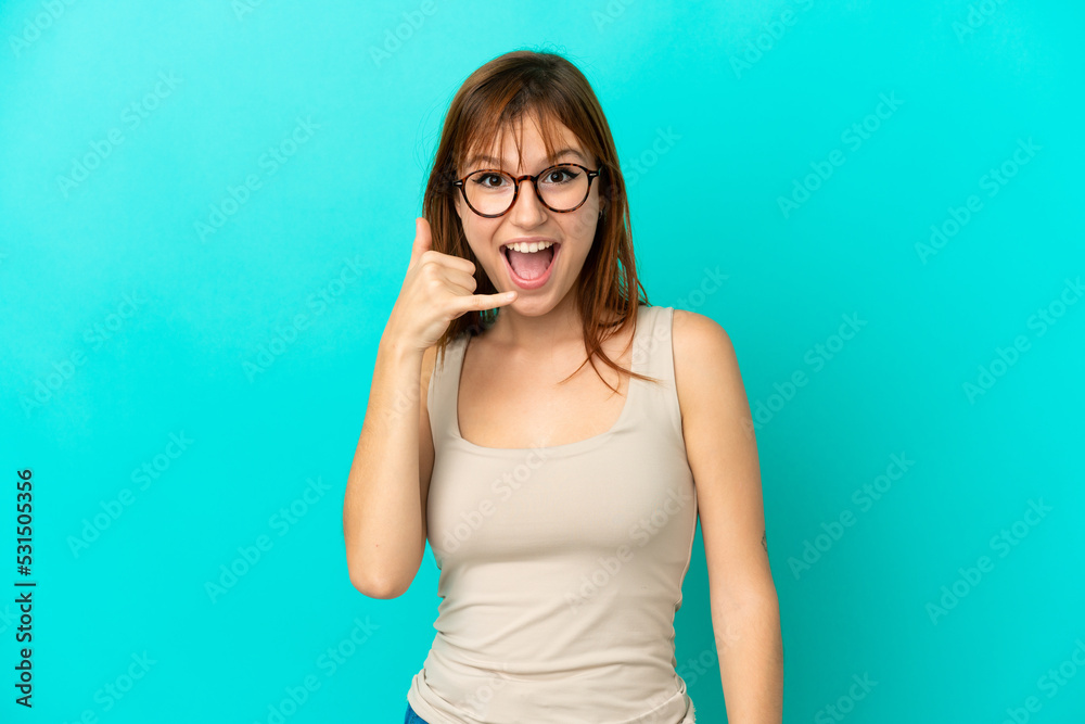 Redhead girl isolated on blue background making phone gesture. Call me back sign Redhead girl isolated on blue background making phone gesture. Call me back sign