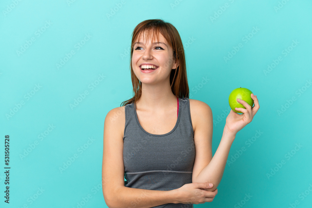 Redhead girl isolated on blue background with an apple and happy Redhead girl isolated on blue background with an apple and happy