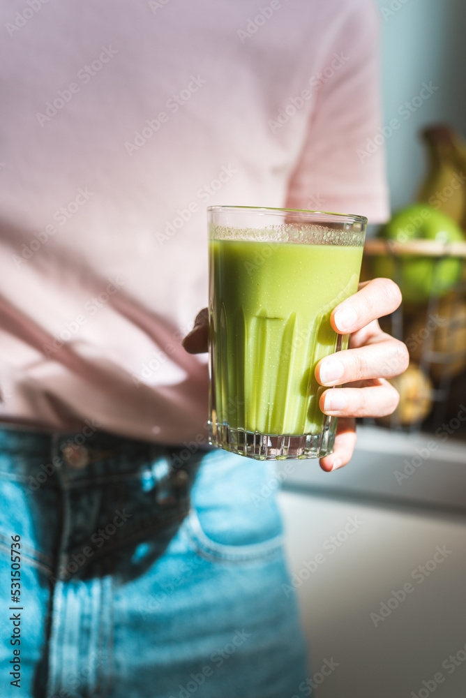 Unrecognizable female hand holding a glass of fresh green healthy smoothie. Unrecognizable female hand holding a glass of fresh green healthy smoothie.