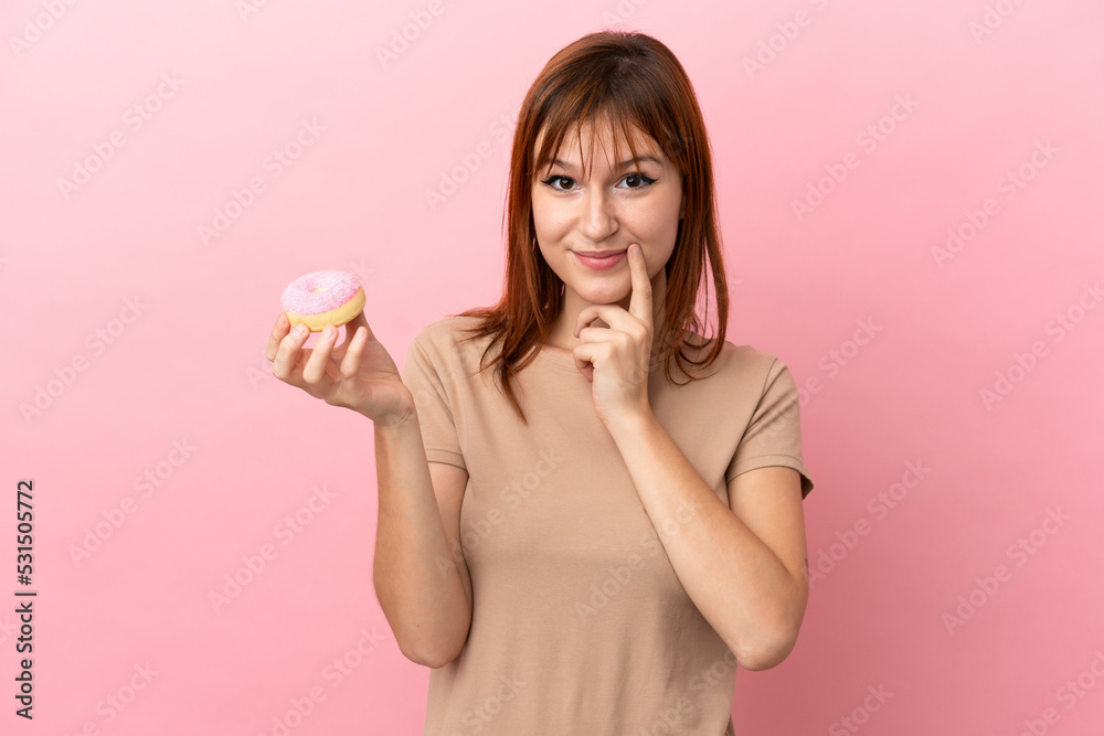 Redhead girl isolated on pink background holding a donut Redhead girl isolated on pink background holding a donut