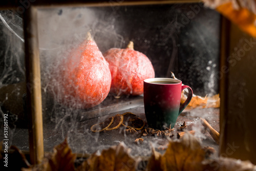 halloween concept, hot tea with spices inside the window and pumpkin on a dark background