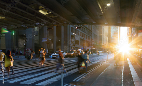 Sunlight shining on people walking across a busy street crosswalk at Grand Central Station in Manhattan New York City photo